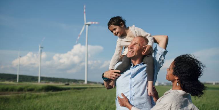Two adults and a child in a field wind turbines in background