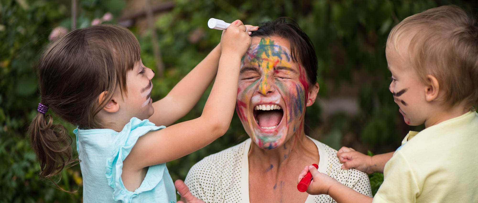 Two young children drawing on a laughing woman