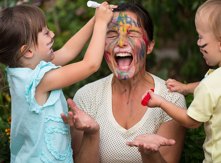 Two children putting facepaint on Mum