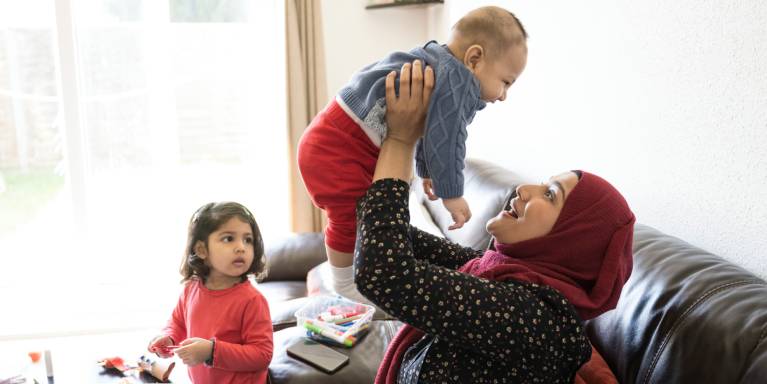 Woman holding baby up in the air while toddler watches