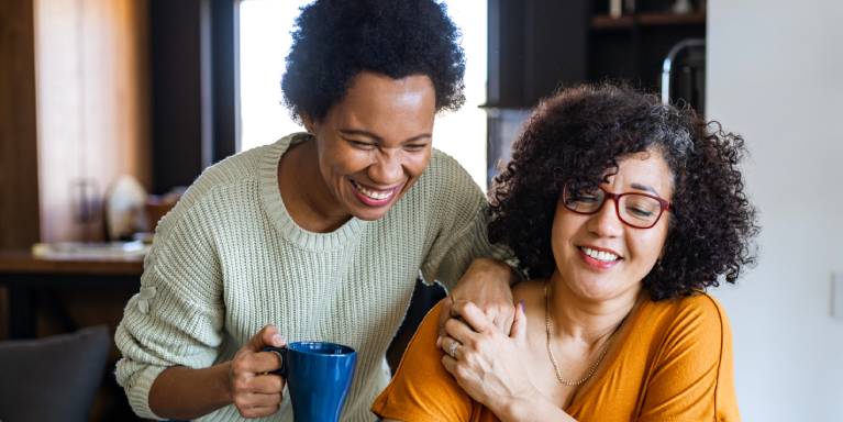 Two women smiling holding hands looking at laptop