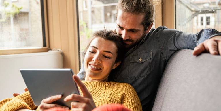 Smiling man and woman sat on sofa looking at laptop