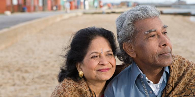 Older man and woman sat on beach looking into the distance