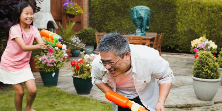 Laughing man and child using water pistols in the garden