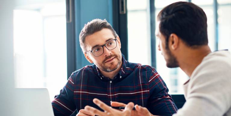 Two men talking and using laptop